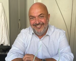 Hombre sonriente con camisa blanca sosteniendo gafas