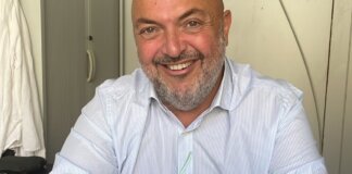 Hombre sonriente con camisa blanca sosteniendo gafas