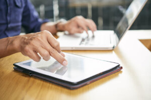 Persona usando una tablet y una laptop en una mesa de madera