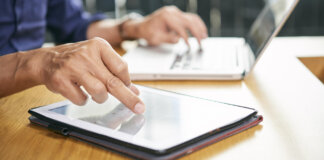 Persona usando una tablet y una laptop en una mesa de madera