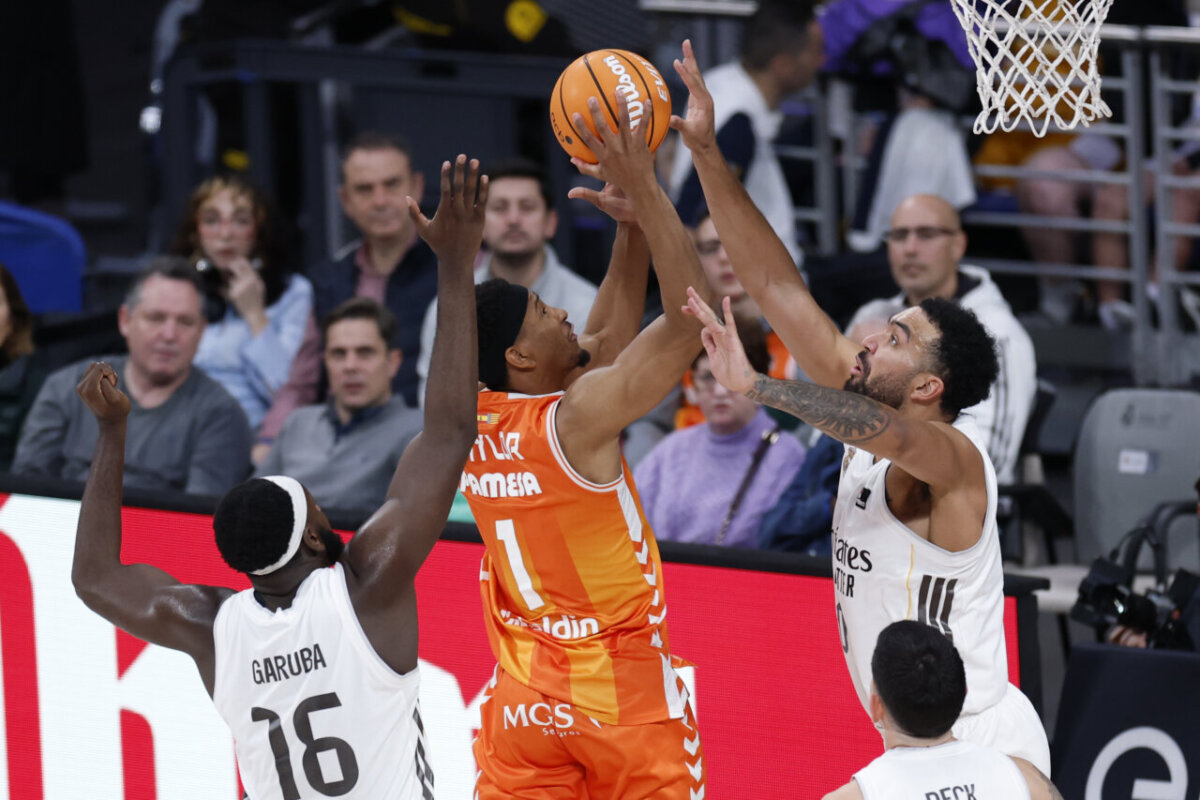 Jugador de Valencia Basket intenta anotar mientras dos defensores del Real Madrid lo bloquean.