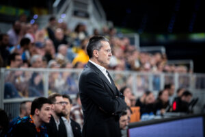 Entrenador Pedro Martínez observando un partido de baloncesto con seriedad.