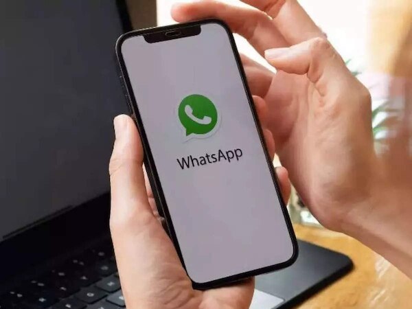 Persona usando WhatsApp en un teléfono móvil junto a una laptop