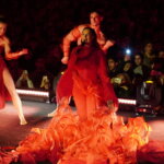 Artista en un espectáculo con vestuario rojo y bailarines en escena