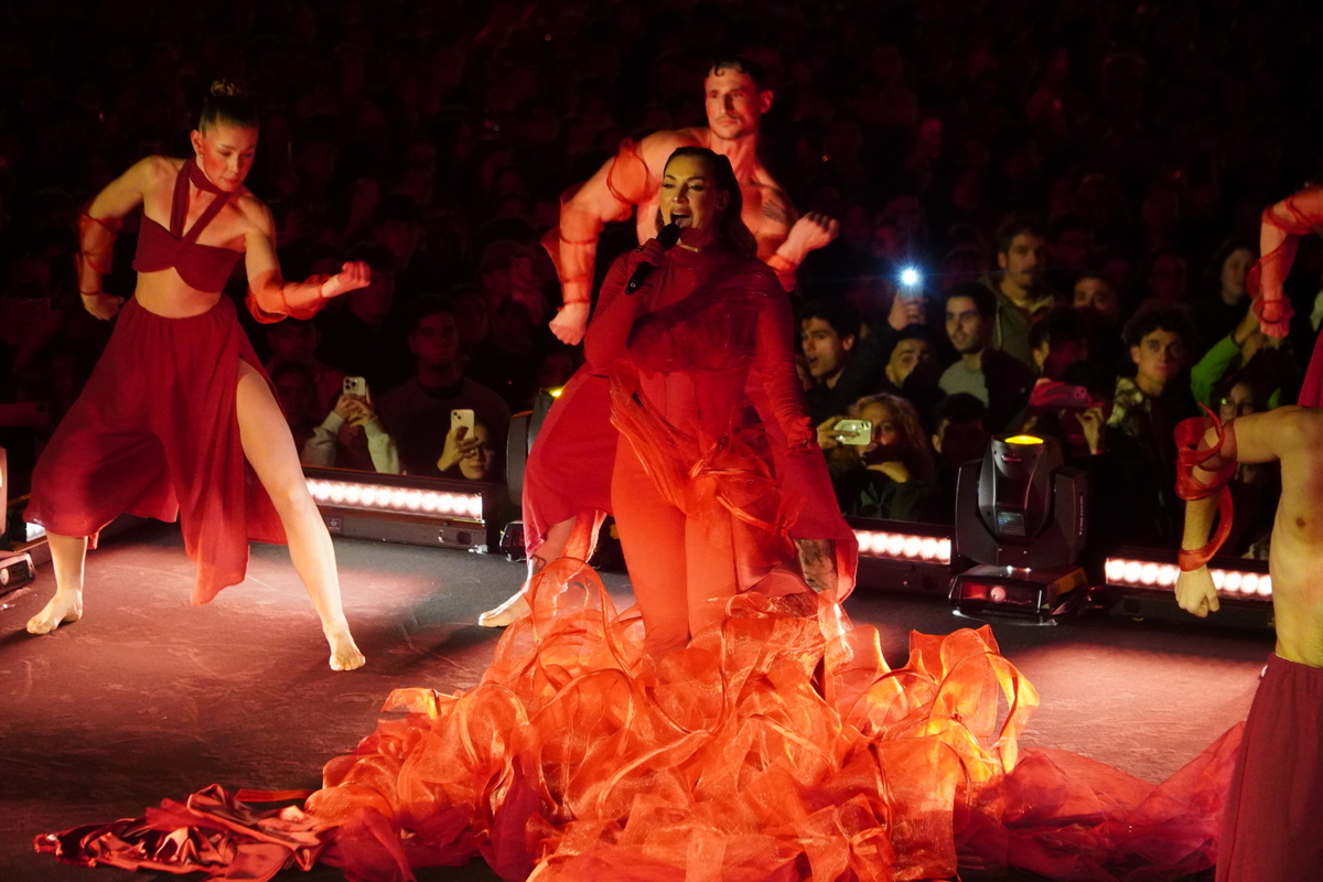 Artista en un espectáculo con vestuario rojo y bailarines en escena
