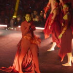 Artista actuando en el escenario con vestuario rojo y bailarines