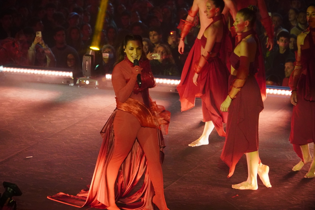 Artista actuando en el escenario con vestuario rojo y bailarines