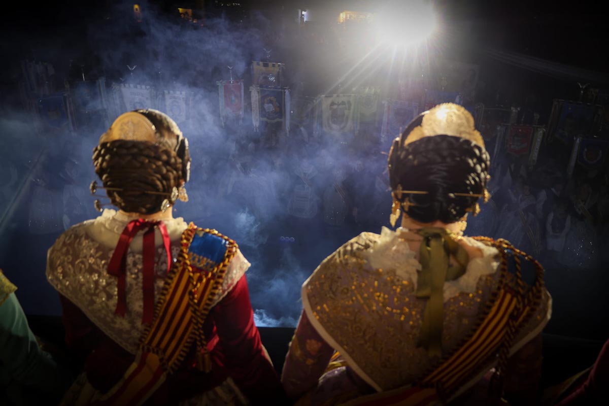 Dos falleras observando el evento Crida de Torrent con banderas de fondo