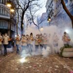 Grupo de personas con trajes blancos en un desfile festivo con humo