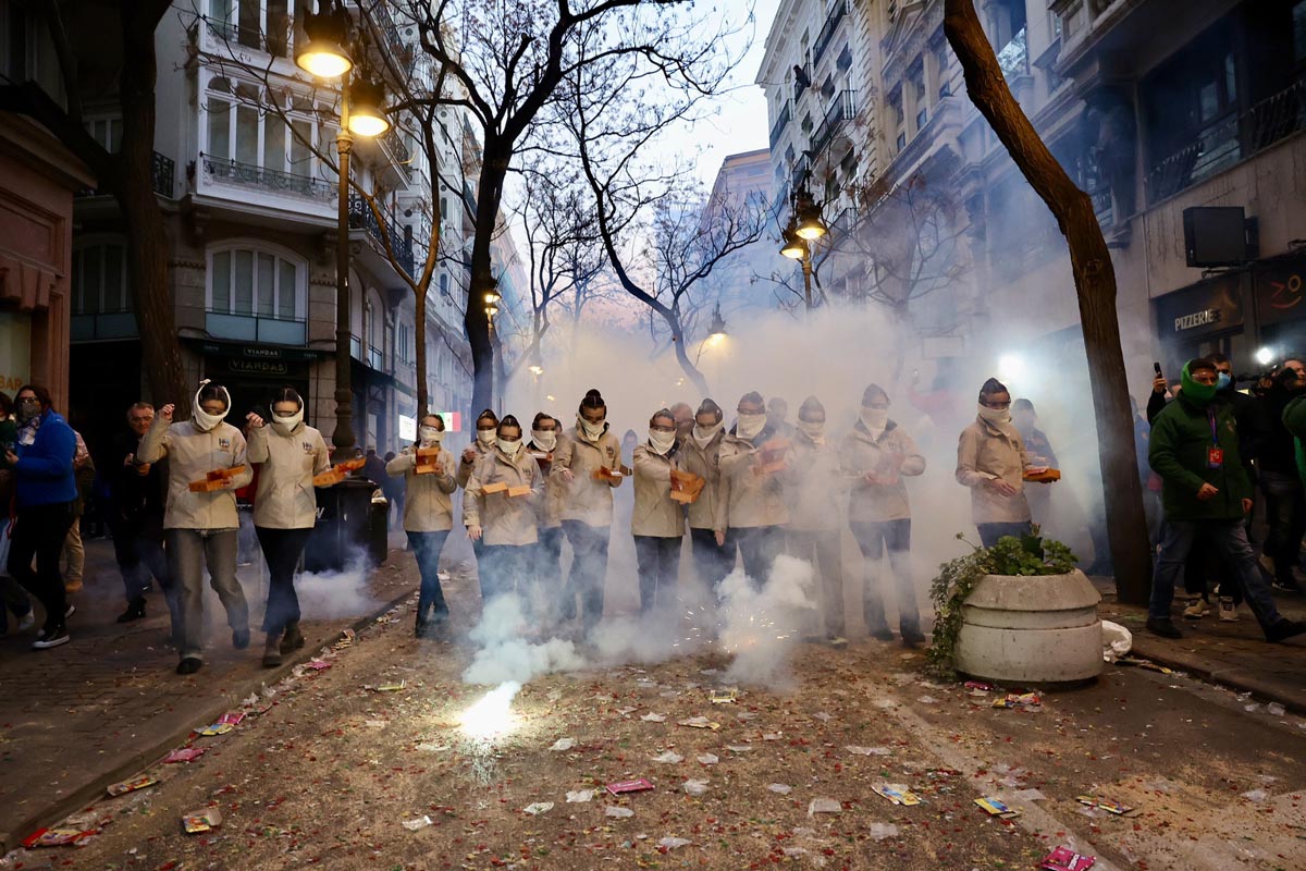 Grupo de personas con trajes blancos en un desfile festivo con humo