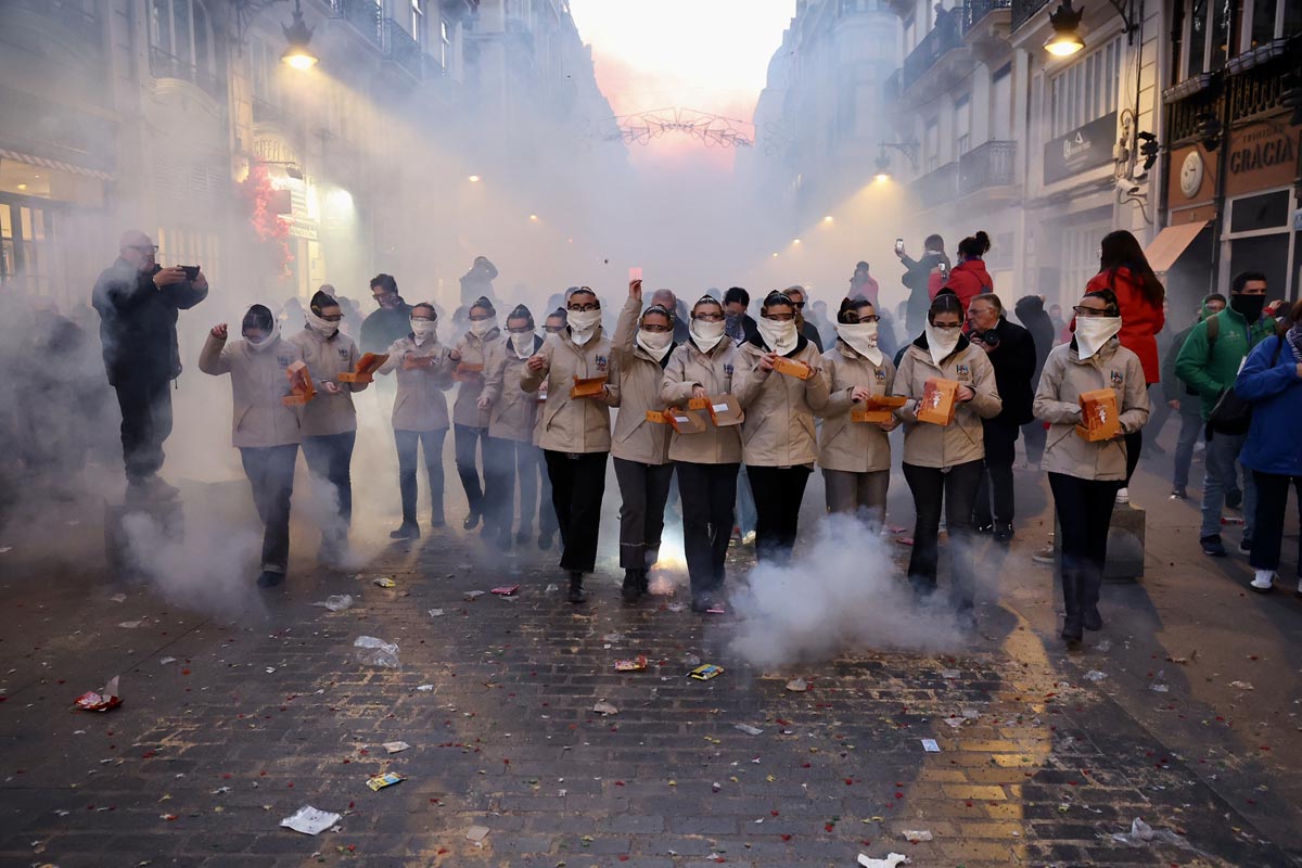 Grupo de personas en un desfile festivo con humo y confeti en la calle.