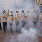 Grupo de personas con mascarillas en un desfile con humo y fuegos artificiales