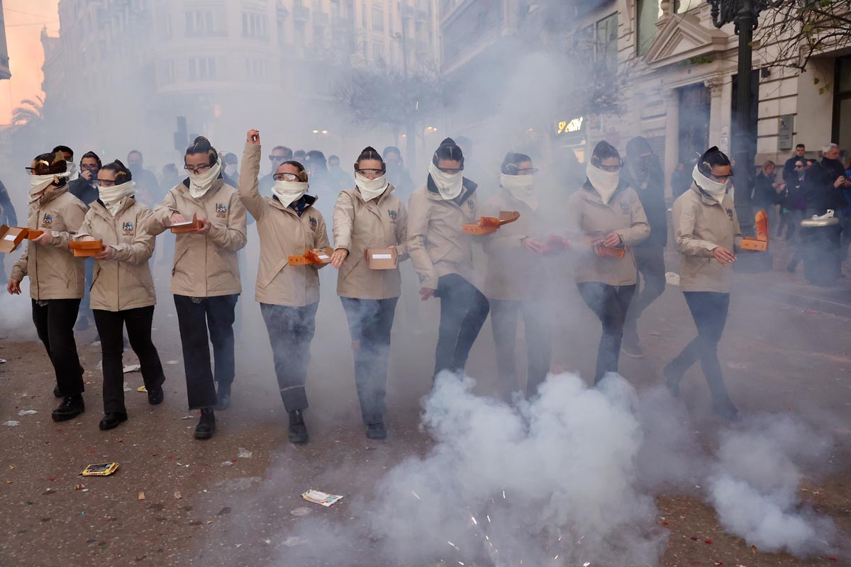 Grupo de personas con mascarillas en un desfile con humo y fuegos artificiales