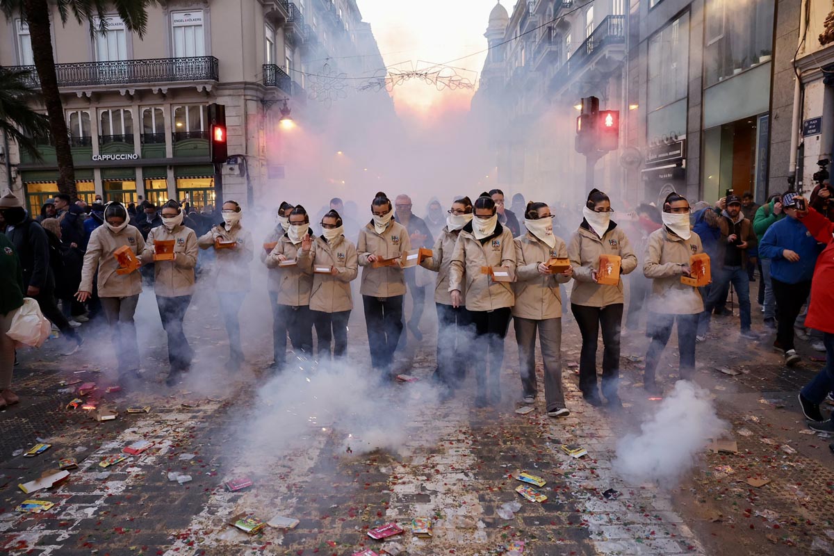 Grupo de personas con mascarillas en un desfile con humo y fuegos artificiales.