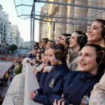Mujeres sonriendo en un balcón durante un desfile en la ciudad.