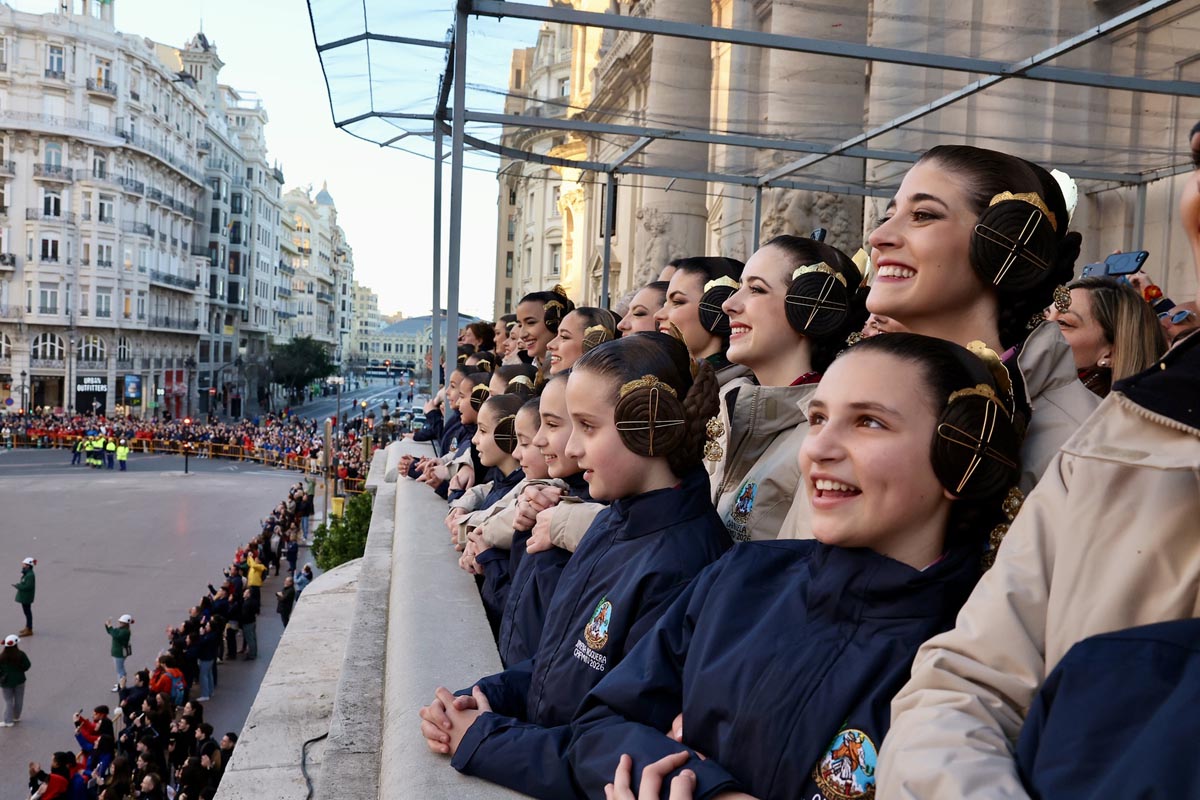 Mujeres sonriendo en un balcón durante un desfile en la ciudad.