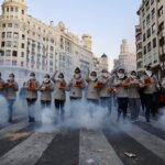 Grupo de personas en un desfile tradicional en Valencia con humo y confeti.