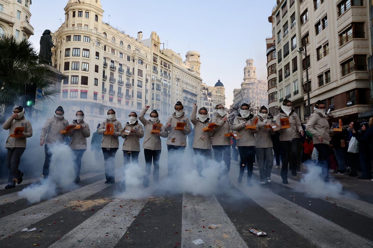 Grupo de personas en un desfile tradicional en Valencia con humo y confeti.