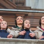 Mujeres y niñas con trajes tradicionales observando un evento