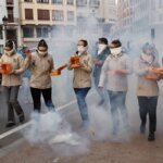 Mujeres en un desfile sosteniendo cajas en medio de humo