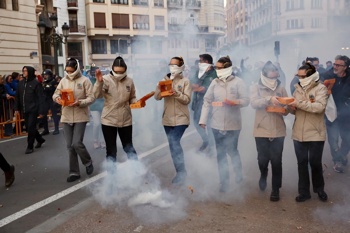 Mujeres en un desfile sosteniendo cajas en medio de humo