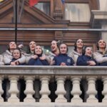 Grupo de mujeres y niñas sonriendo desde un balcón