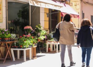 Dos personas caminando junto a una floristería con plantas coloridas
