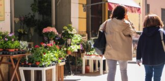 Dos personas caminando junto a una floristería con plantas coloridas