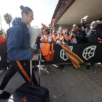 Jugadora de Valencia Basket llegando con maleta mientras aficionados celebran.
