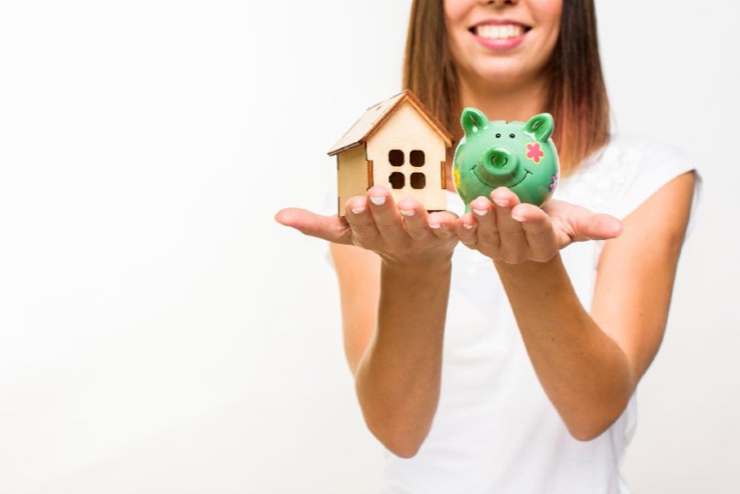 Mujer sosteniendo una casa de madera y una alcancía verde