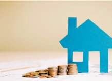 Modelo de casa de papel junto a monedas en una mesa