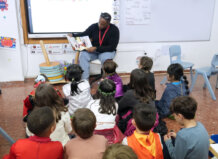 Un hombre lee un libro a un grupo de niños en un aula