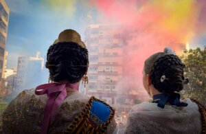 Dos falleras observando una mascletà en Torrent con humo de colores