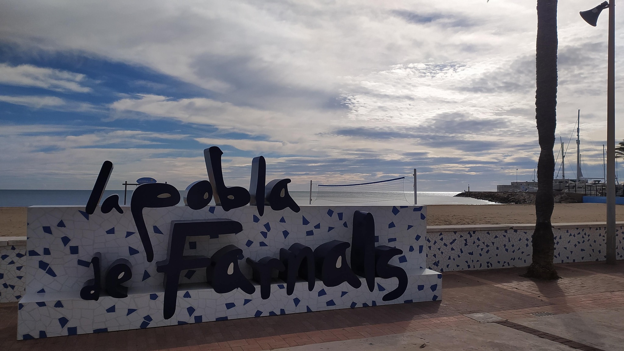 Cartel de la Pobla de Farnals junto a la playa con cielo nublado