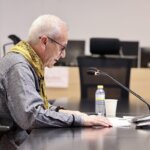 Hombre leyendo en una mesa con micrófono y botellas de agua