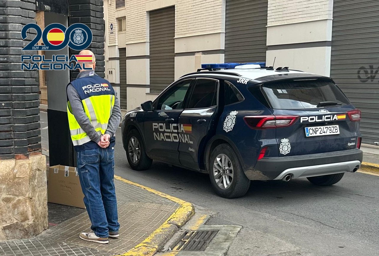 Agente de policía nacional junto a un coche patrulla en la calle