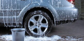 Coche plateado siendo lavado a mano con espuma y cubo.