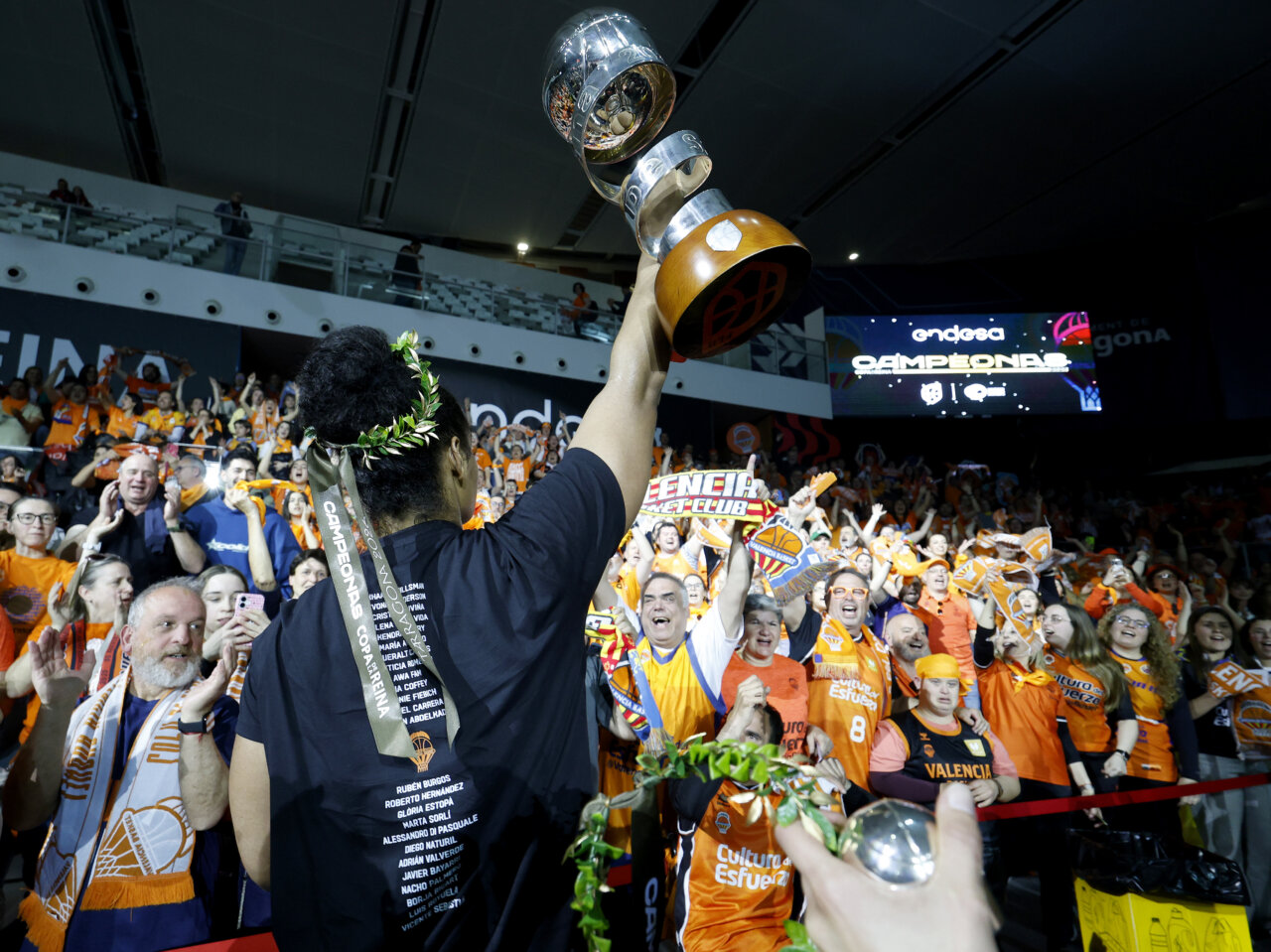 Jugadora de Valencia Basket levantando el trofeo con aficionados celebrando.