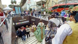 Personas en trajes tradicionales accediendo a la estación de metro Ángel Guimerá durante las Fallas.