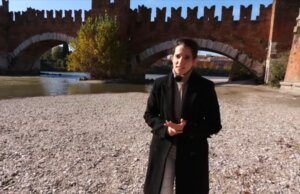 Mujer en la orilla de un río con un puente de fondo