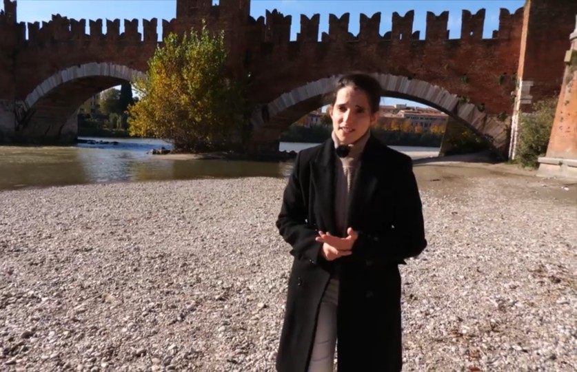 Mujer en la orilla de un río con un puente de fondo