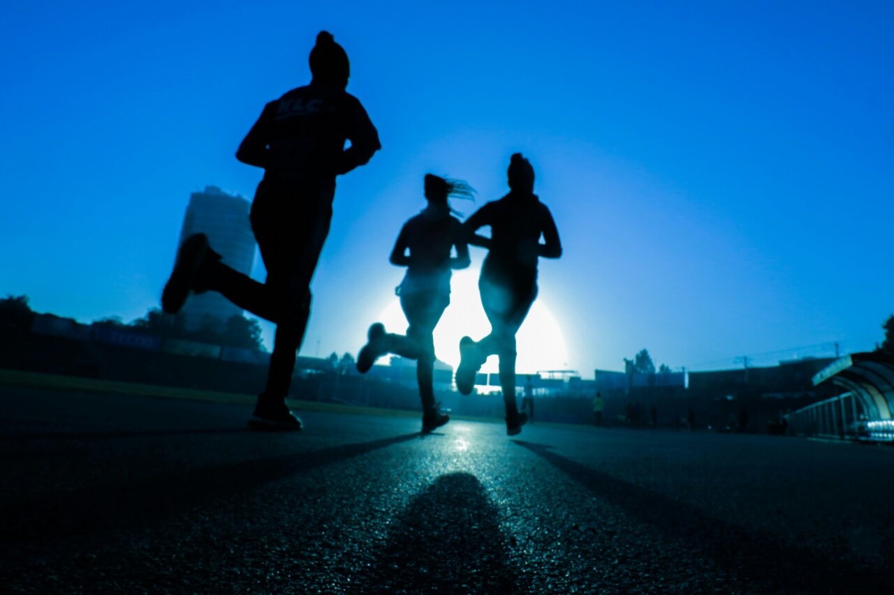 Tres corredores en silueta corriendo al amanecer en una pista