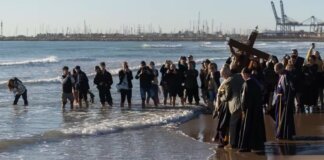 Ceremonia en la playa con imágenes religiosas y fieles rindiendo homenaje