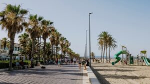 Paseo en la playa de Malva-Rosa con palmeras y gente disfrutando.