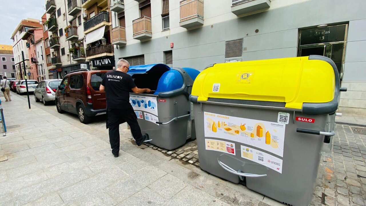 Persona depositando residuos en contenedores de reciclaje en la calle
