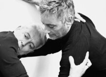 Dos hombres en una coreografía frente a una pared blanca.
