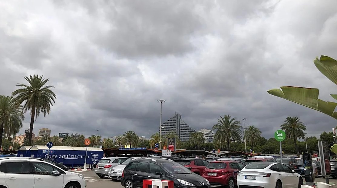 Cielo nublado con palmeras y coches en un aparcamiento