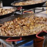Paellas cocinándose en el evento TastArròs en Valencia con carne y verduras.