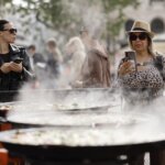Dos mujeres observando la preparación de paellas en el TastArròs en Valencia