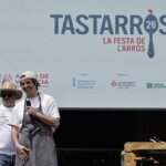 Dos chefs en el evento TastArròs en València, con un gran cartel detrás.